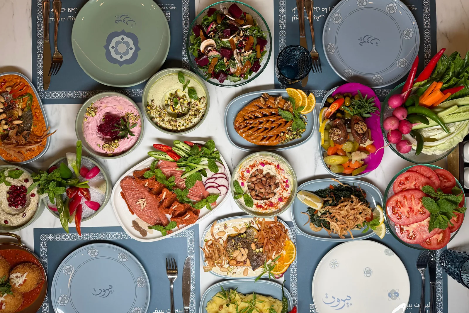 An overhead view of a Middle Eastern mezze spread with dips, salads and grilled dishes (representative photograph of the style of food, not Al Hadheerah's own buffet)