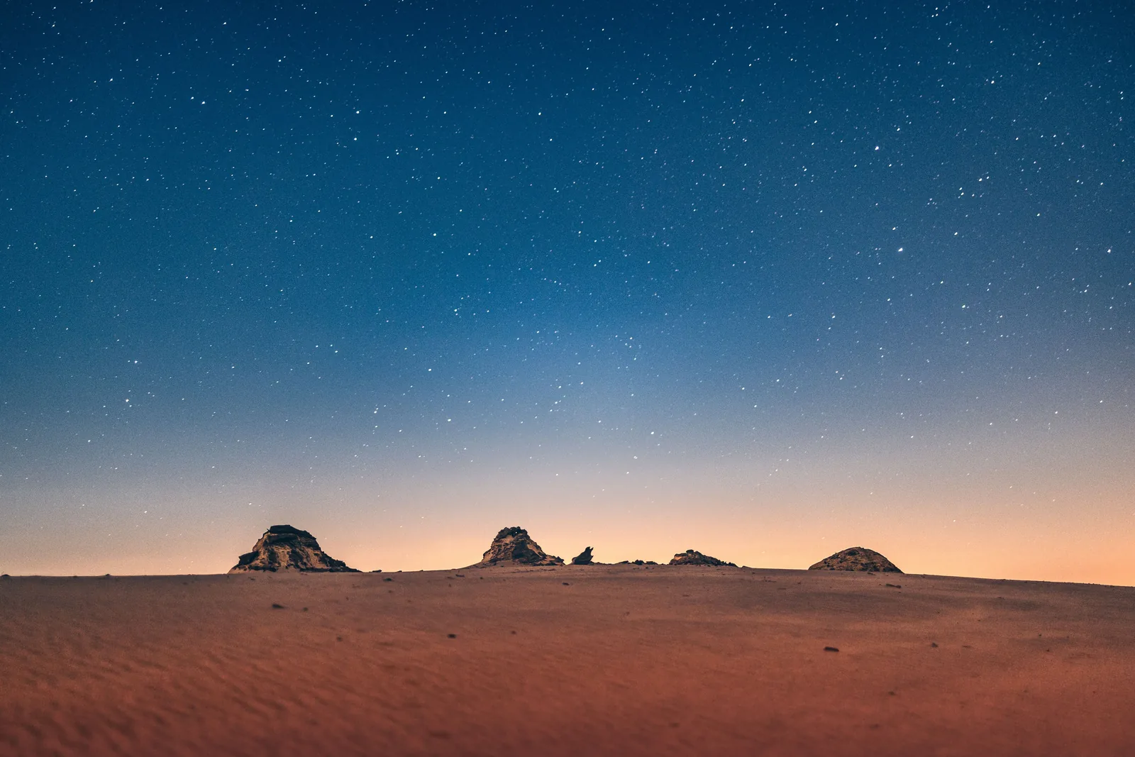 A starry night sky over dark desert dunes and low rock outcrops (representative photograph of a desert night sky)